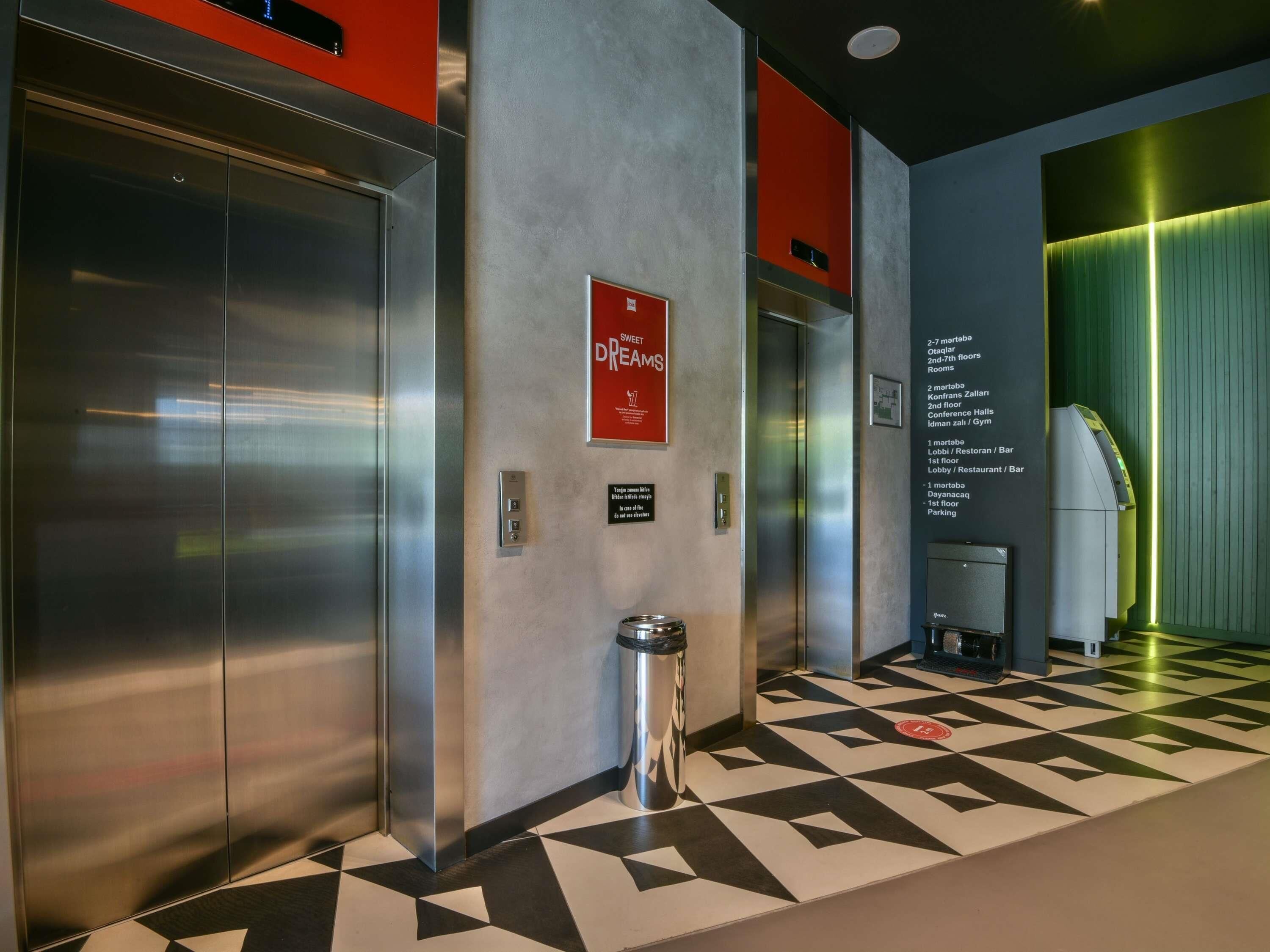 A modern elevator with a red sign, a trash bin, and a floor plan on the wall.