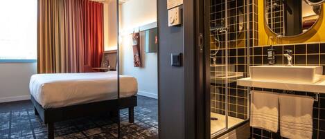 A hotel room with a bed, a bathroom with a sink and mirror, and a window with curtains.