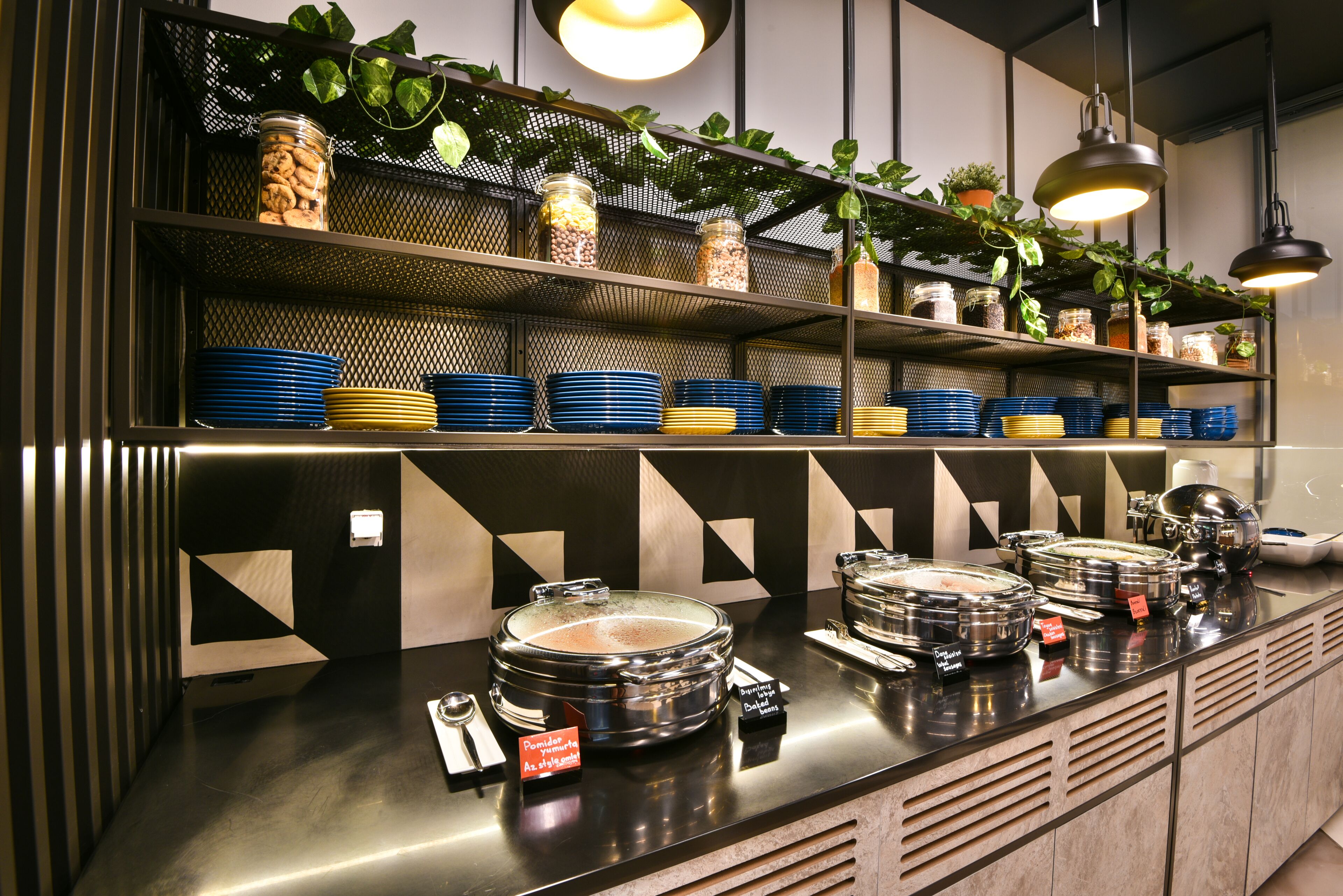 A buffet setup with multiple serving stations, a variety of food containers, and decorative plants.