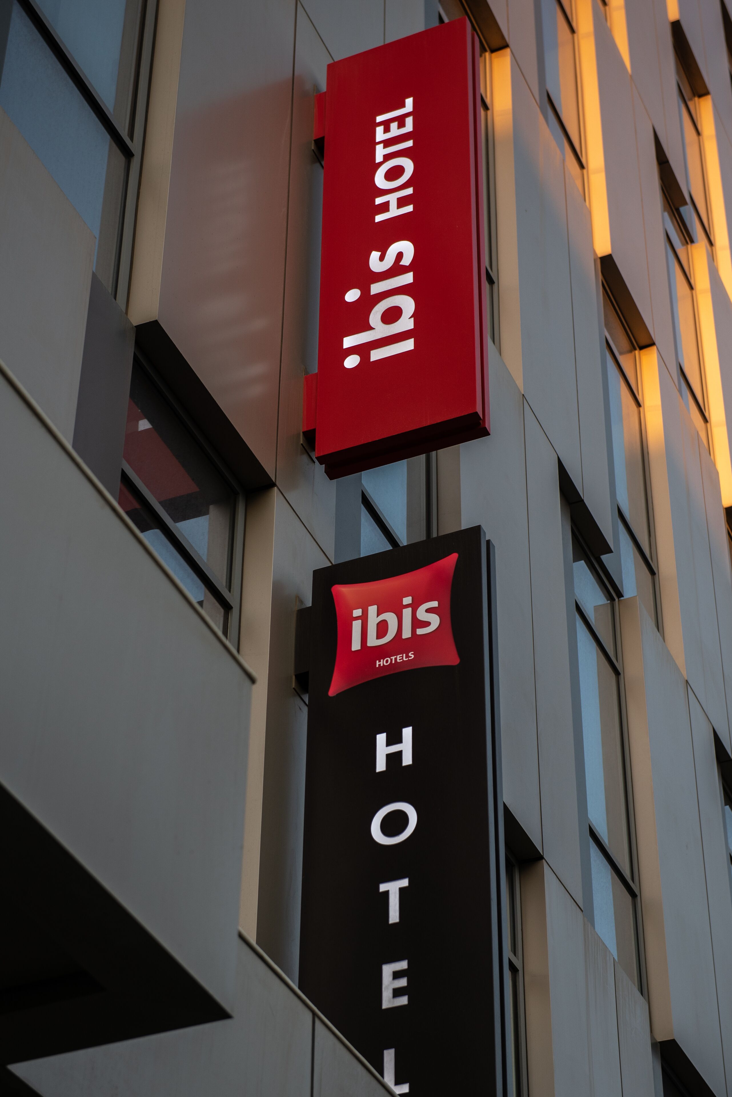 Une enseigne d’hôtel avec le nom « Ibis Hotel » en lettres blanches sur un fond noir, et une banderole rouge au-dessus, portant le même nom en lettres blanches.