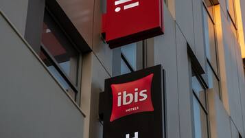 Une enseigne d’hôtel avec le nom « Ibis Hotel » en lettres blanches sur un fond noir, et une banderole rouge au-dessus, portant le même nom en lettres blanches.