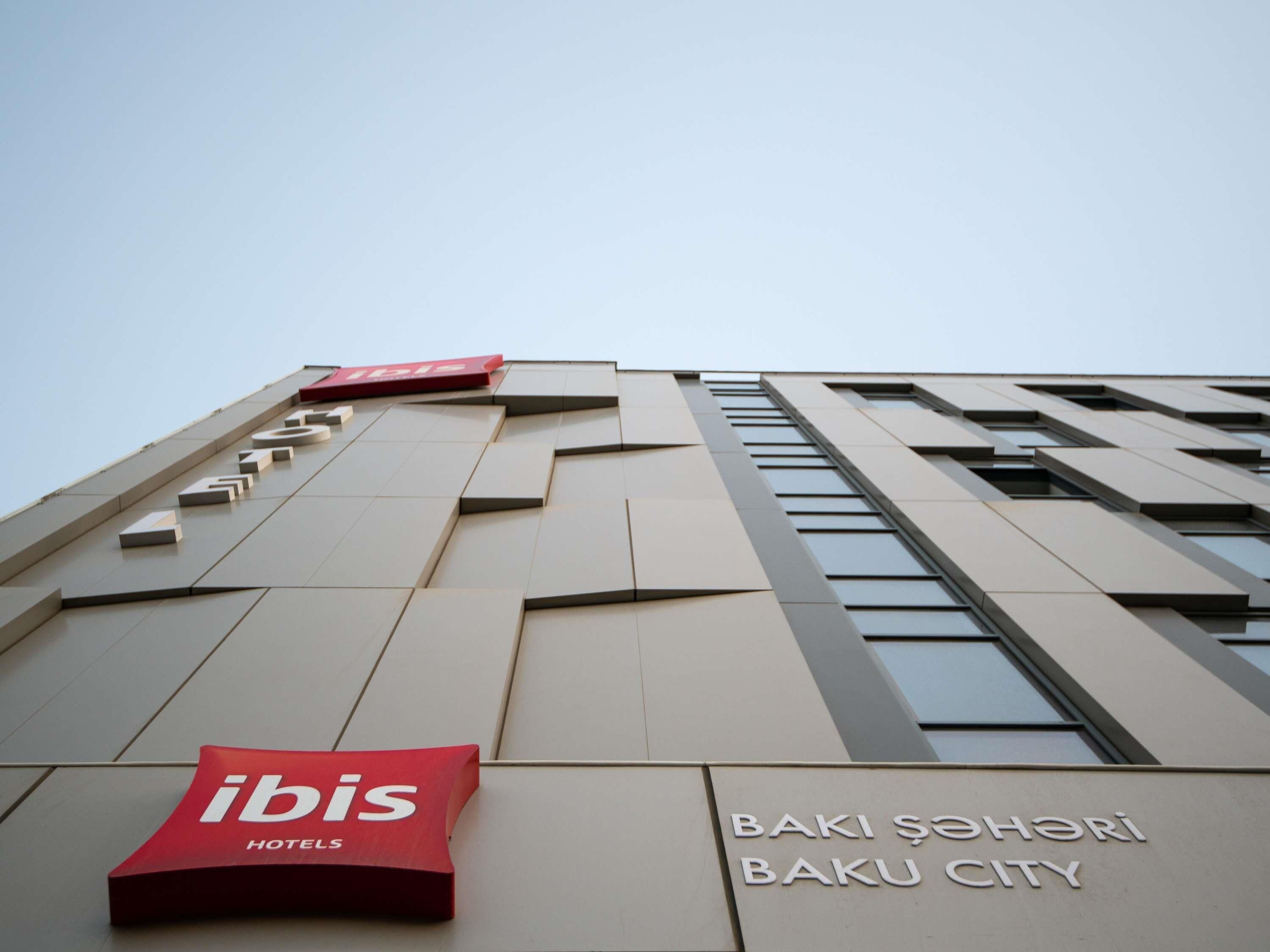Ein Hotelgebäude mit modernem Design, das ein gut sichtbares 'ibis Hotels'-Schild und die Aufschrift 'BAKI ŞAHERI BAKU CITY' an der Fassade zeigt.