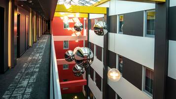 Een modern gebouw met een gevel in rood en wit, meerdere verdiepingen en een centraal atrium met een glazen dak.