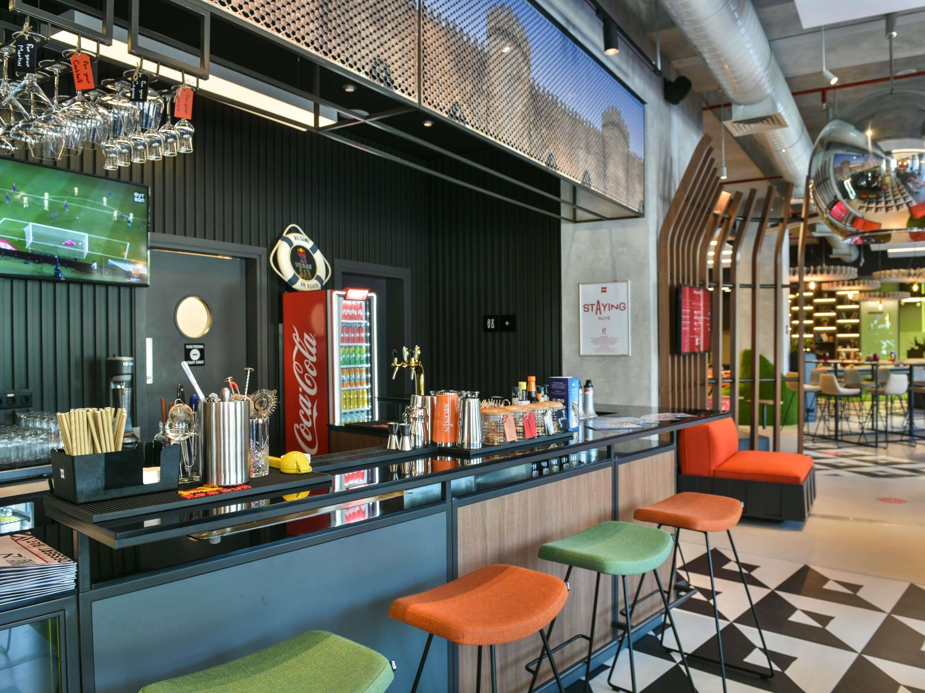 A bar area with stools, a Coca-Cola refrigerator, and various bar tools.