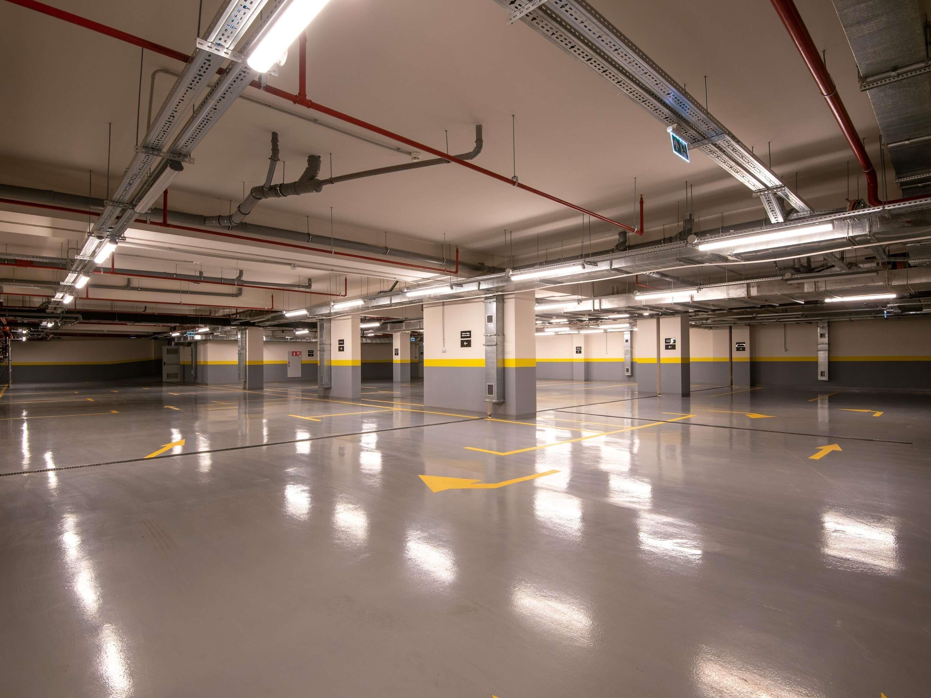 A clean, well-lit parking garage with clear directional arrows on the floor, multiple parking spaces, and visible structural elements like beams and columns.