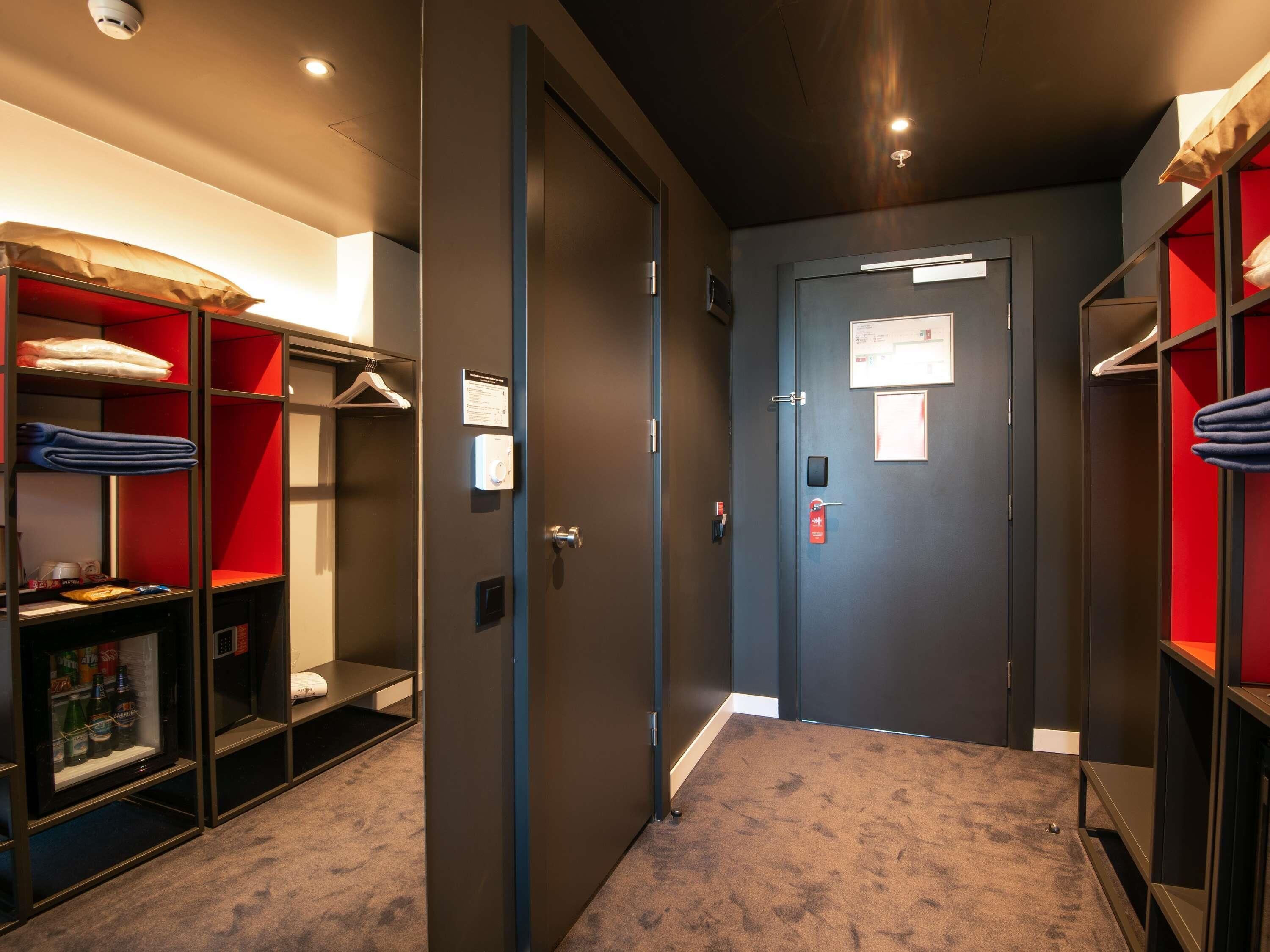Un couloir d’hôtel avec une porte, un porte-manteau et une étagère où sont pliées des serviettes.