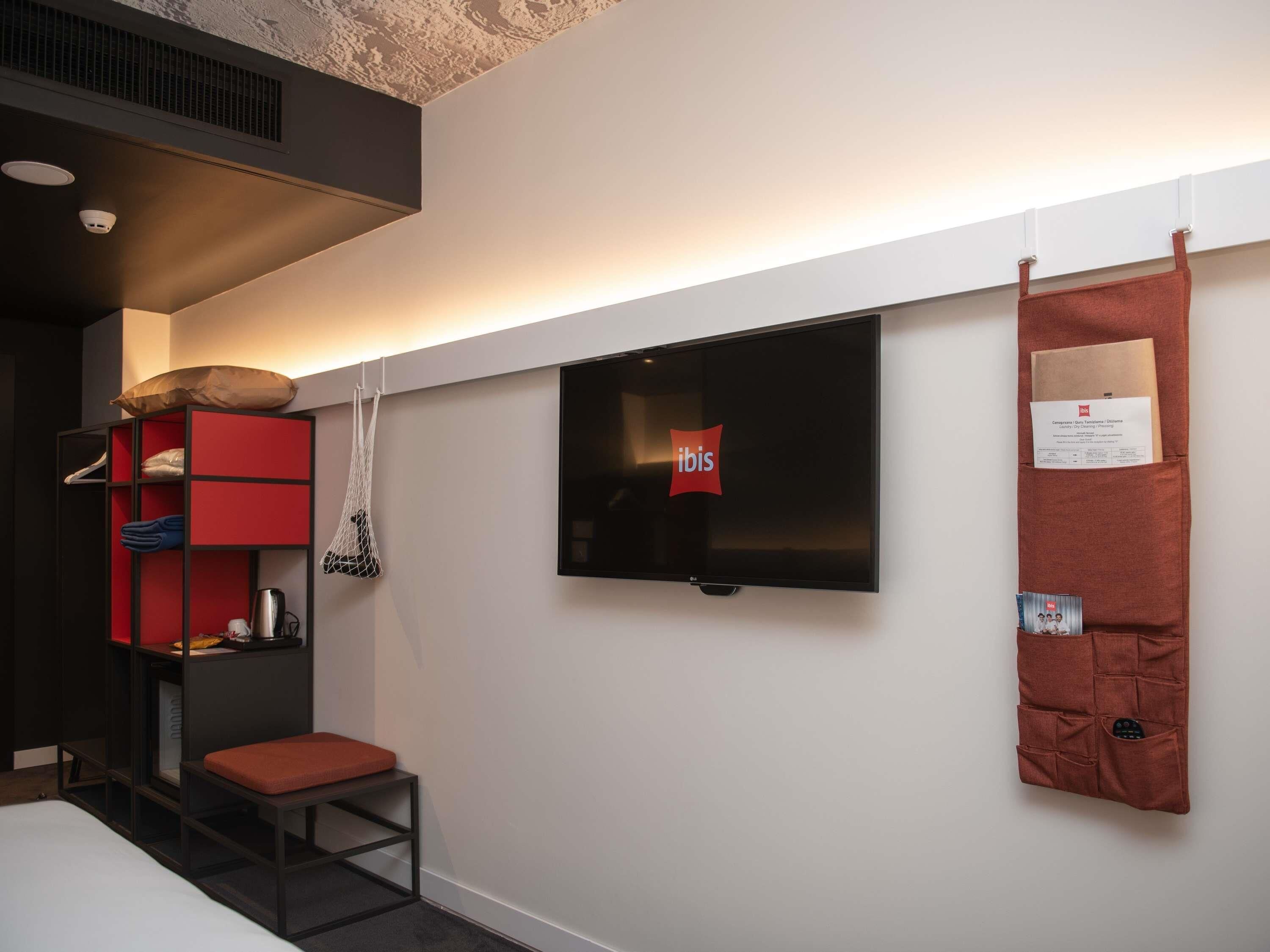 A modern room with a bed, a red and black storage unit, a television, and a bulletin board.