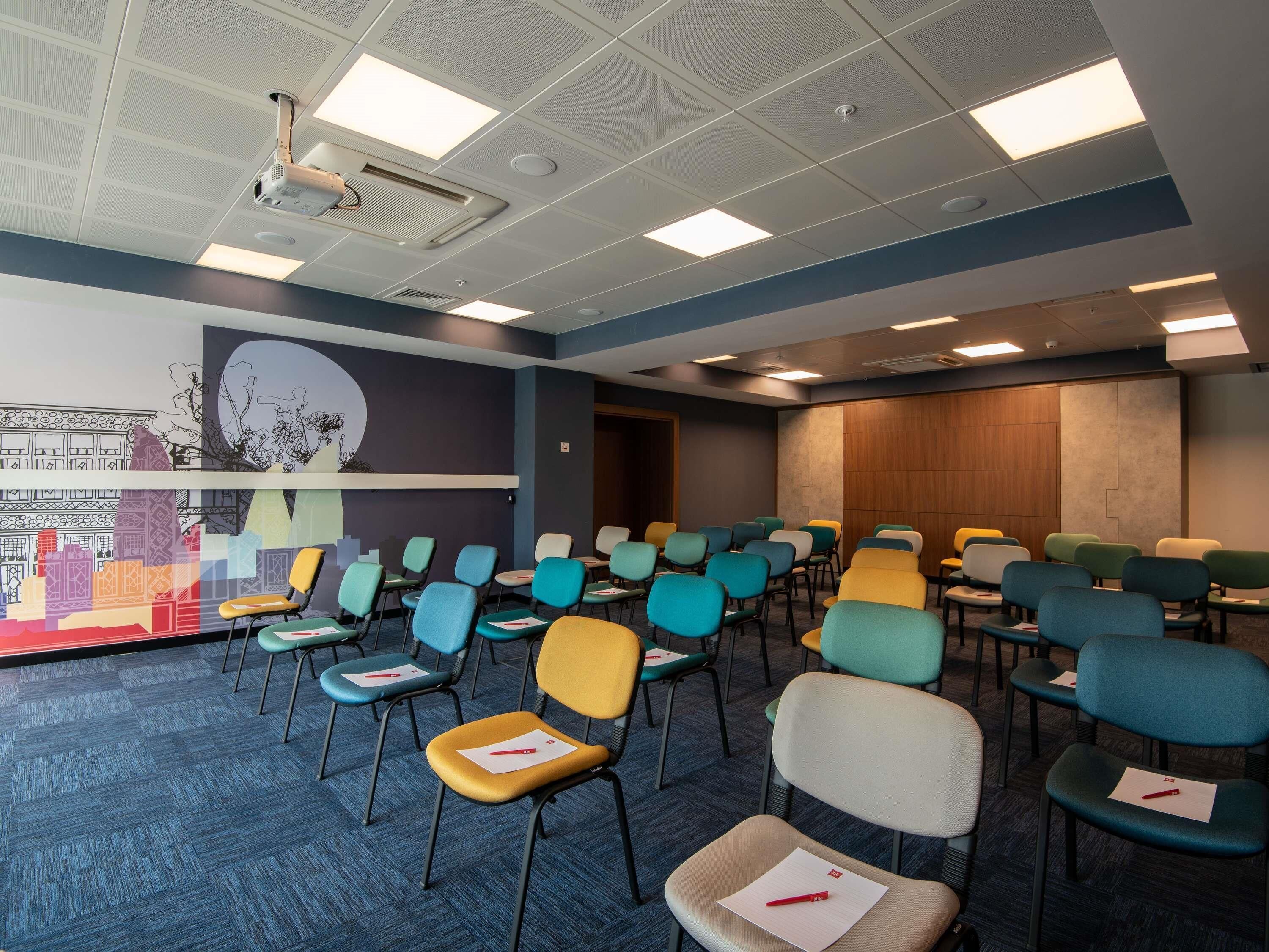 Een congreszaal met rijen stoelen, een projecteerder en een groot muurdecor.