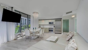 A modern living room with a large TV, a dining area, and a kitchen.