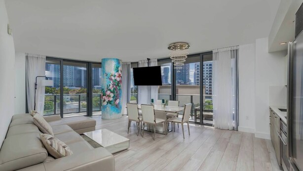 A modern living room with a sofa, dining table, and chairs, a large window with a city view, and a decorative pillar.