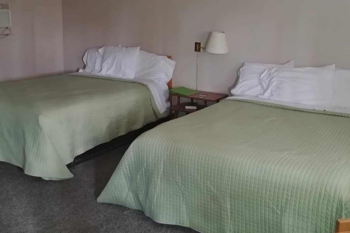A hotel room with two single beds, a ceiling fan, a bedside table with a lamp, and a small wooden table.