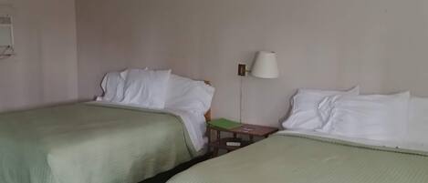 Une chambre d’hôtel avec deux lits simples, un ventilateur de plafond, une table de chevet avec une lampe et une petite table en bois.