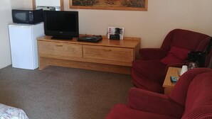 A room with a wooden cabinet, a television, a microwave, a refrigerator, a red sofa, a coffee table, and a painting of a desert landscape. - Cactus Inn (McLean)