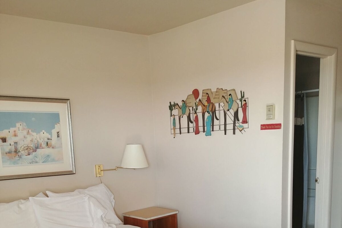A hotel room with a bed, a nightstand, a lamp, a painting, and a wall decoration.