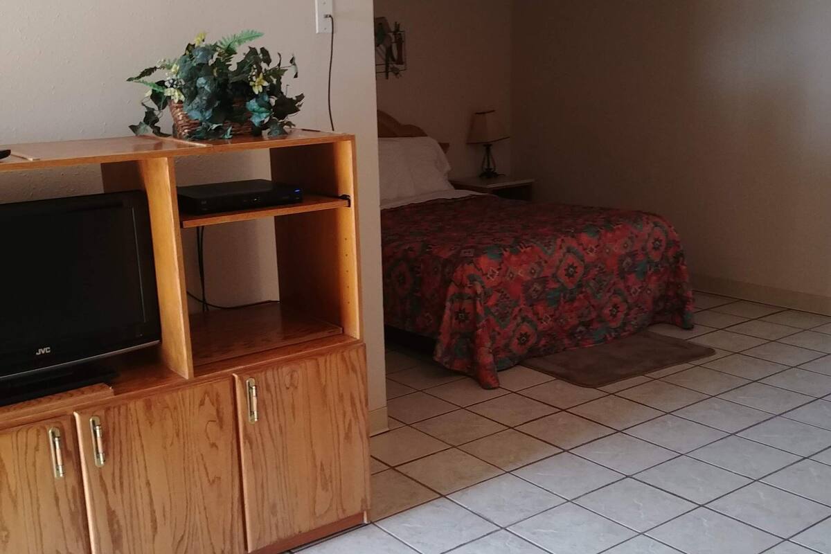 A room with a wooden entertainment unit, a bed with a patterned bedspread, and a tiled floor.