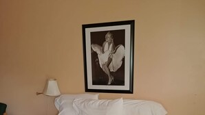 A neatly made bed with a grey quilt, a framed picture on the wall, a bedside lamp, and a wooden nightstand. - Cactus Inn (McLean)