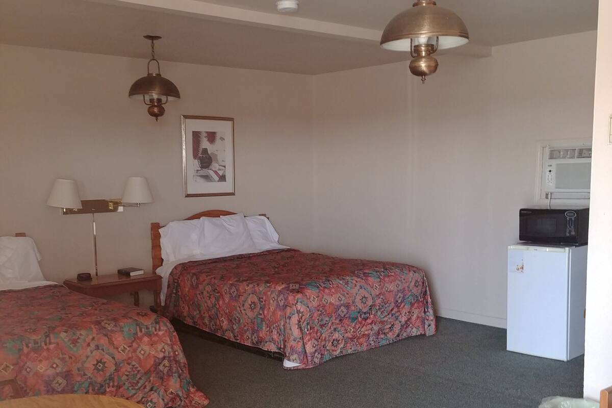A hotel room with two beds, a desk, a chair, a microwave, and a trash bin.