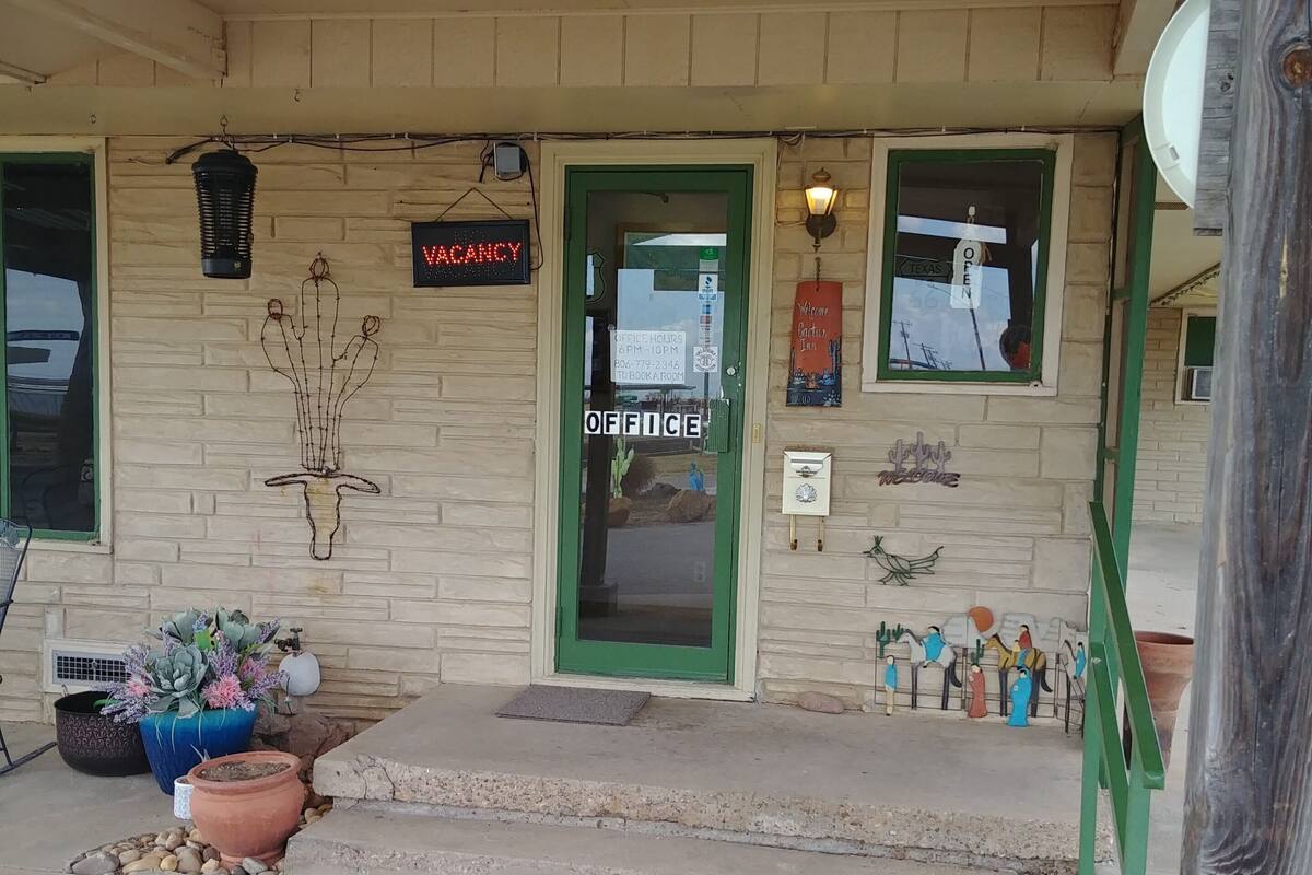 A building with a green door, a 'VACANCY' sign, and a 'TEXAS OPEN' sign.