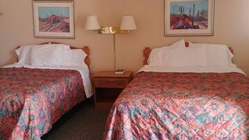 Een hotelkamer met twee bedden, elk voorzien van beddengoed met een patroon, een nachtkastje met een lamp, en twee ingelijste schilderijen aan de muur.