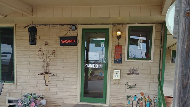 A building with a green door, a sign indicating office hours, and a 'VACANCY' sign. - Cactus Inn (McLean)