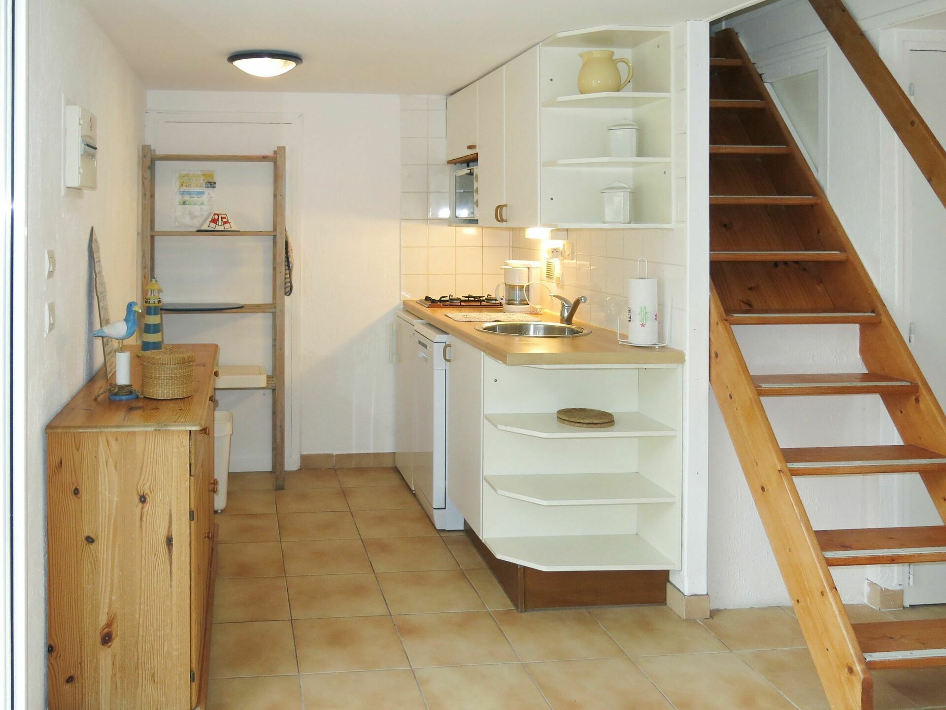 Eine kleine Küche mit Holztischplatte, Spüle und integriertem Herd. Eine Holztreppe führt zu einer oberen Ebene.