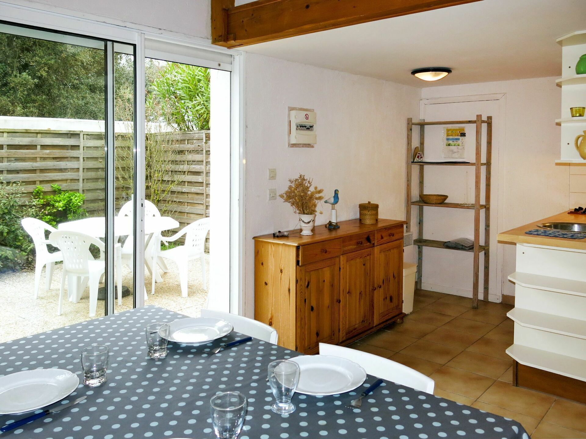 A dining area with a table set for four, a wooden cabinet, and a kitchen area with a ladder and shelves.