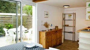 Un coin repas avec une table dressée pour quatre personnes, un buffet en bois et un espace cuisine équipé d’une échelle et d’étagères.
