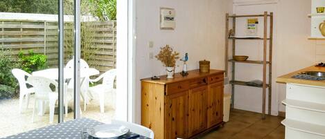 A dining area with a table set for four, a wooden cabinet, and a kitchen area with a ladder and shelves.
