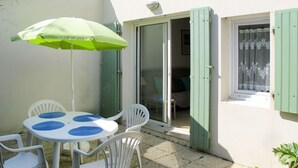 A patio with a table and chairs, a green umbrella, and a sliding glass door leading to a bedroom. - Cosy apartment for 4 people with WIFI, TV and terrace (La Grainetière)