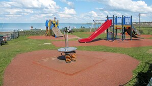 A playground with a red slide and climbing structures, located near a body of water. - Cosy apartment for 4 people with WIFI, TV and terrace (La Grainetière)