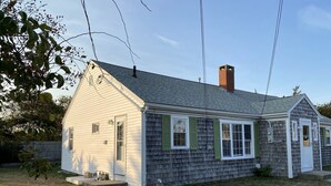 Une maison de plain-pied avec un toit à pignon, une cheminée et un porche à l’avant.