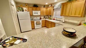 A kitchen with wooden cabinets, a white refrigerator, a microwave, an oven, and a sink. - Perfect Location 2/2 Villa in Creekside Landing walking distance to Lake Sumter (The Villages)