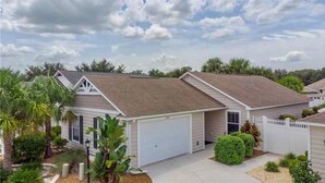 A single-story house with a garage, surrounded by palm trees and a well-maintained lawn. - Perfect Location 2/2 Villa in Creekside Landing walking distance to Lake Sumter (The Villages)
