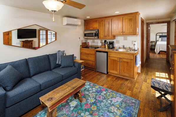 A compact living space with a sofa, a wooden coffee table, a kitchen area with wooden cabinets, a microwave, and a small refrigerator. - Cabin in Downtown Ephraim-Perfect for couples! (Ephraim)
