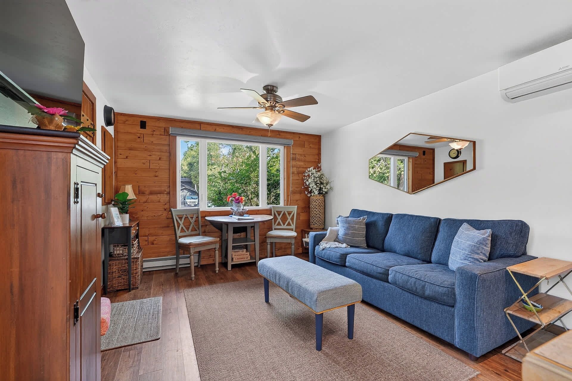 Une pièce avec un canapé bleu, des meubles en bois, une table à manger avec des chaises, un ventilateur de plafond et une grande fenêtre.