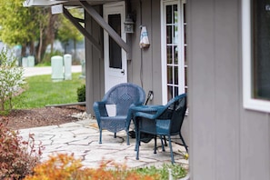 A house exterior with a porch, two wicker chairs, a door, and a window.