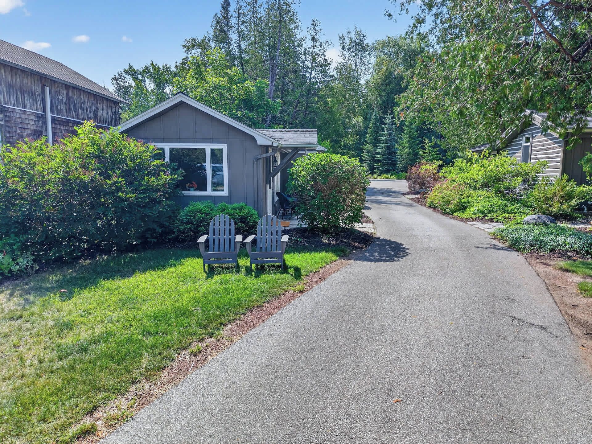 Une allée menant à une maison, avec un porche abrité et deux fauteuils Adirondack.