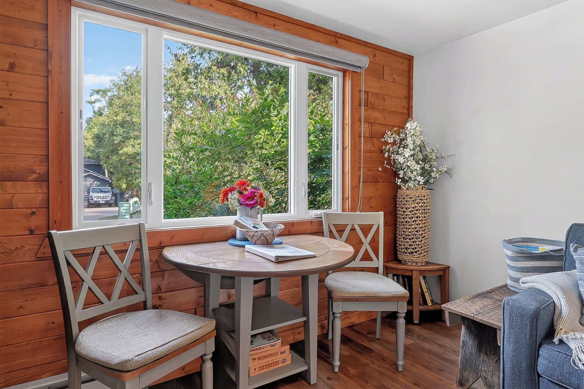 Un coin accueillant avec une table ronde, deux chaises, un panier en osier et une vue sur la verdure à l’extérieur.