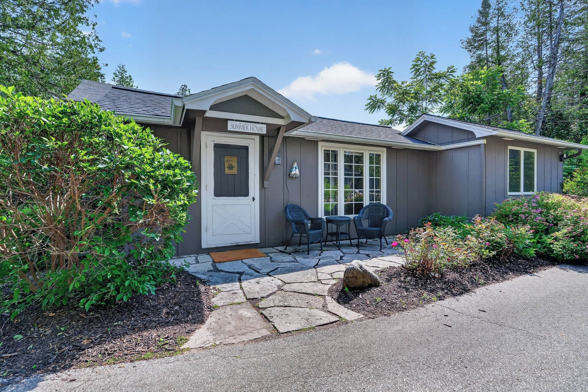 A two-story house with a covered patio, a front door, and a sign that reads 'SUMMER HOUSE.'