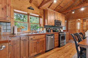 Une cuisine rustique aménagée dans une cabane en bois, avec un four à micro-ondes encastré, des appareils en acier inoxydable et une grande fenêtre.