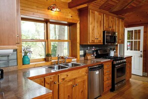 Une cuisine dotĂ©e de meubles en bois, dâun Ă©vier en acier inoxydable, dâun four Ă micro-ondes, dâune cuisiniĂšre et dâun lave-vaisselle.