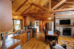 A spacious kitchen with wooden cabinets, a dining area with a table and chairs, and a stone fireplace. - Remodeled Log Cabin | Dog-Friendly Near Wilson's (Ephraim)