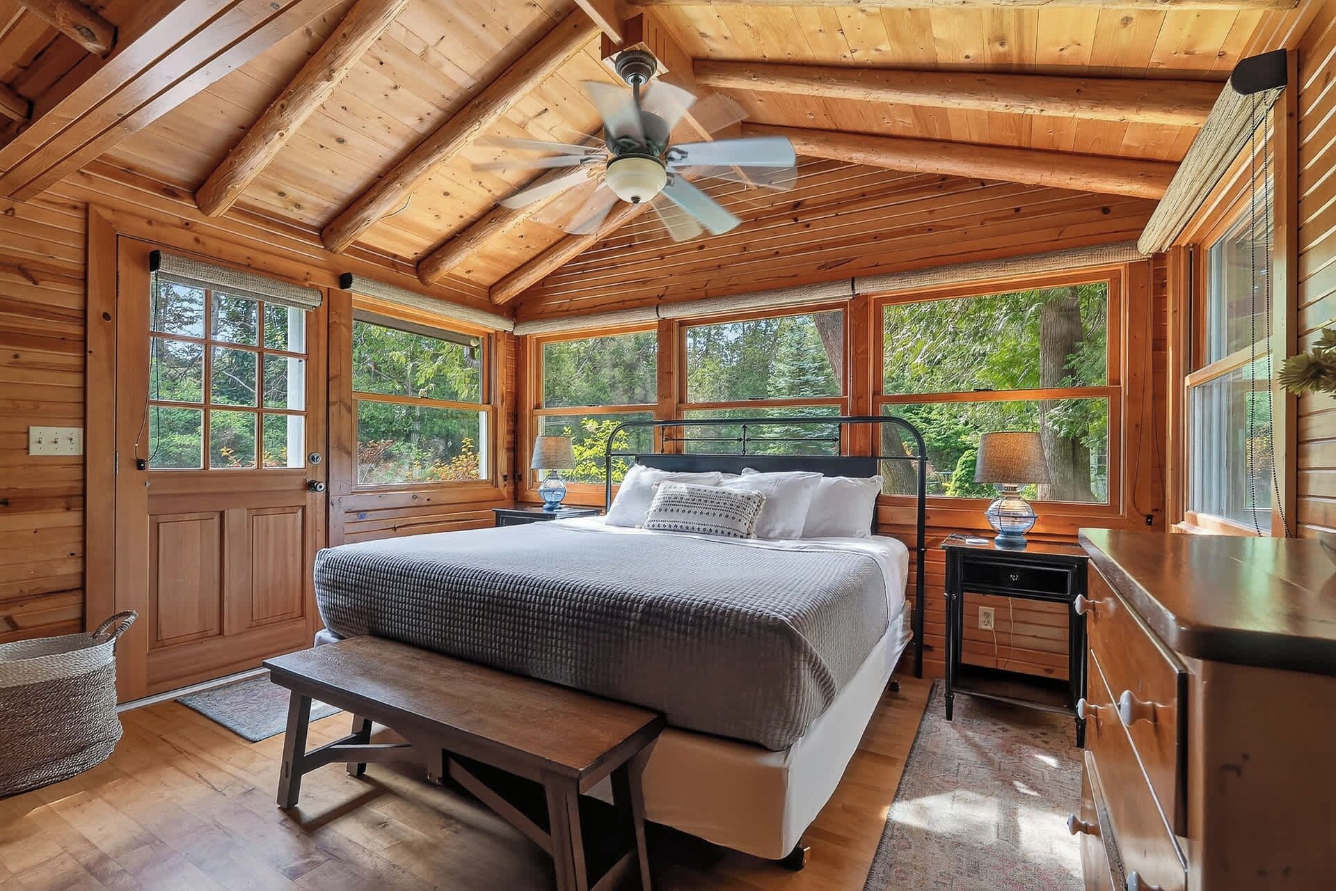 Camera da letto in una casetta di legno con un letto, una panca, un comodino e una ventola a soffitto.
