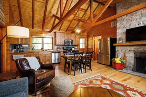 A rustic cabin interior with exposed wooden beams, a stone fireplace, a kitchen with modern appliances, and a cozy seating area. - Remodeled Log Cabin | Dog-Friendly Near Wilson's (Ephraim)