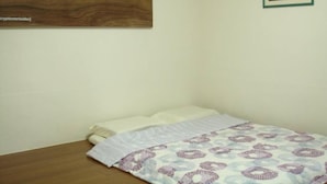Una cama pequeña y ordenada con una colcha estampada, un cabecero de madera y un cuadro enmarcado en la pared.