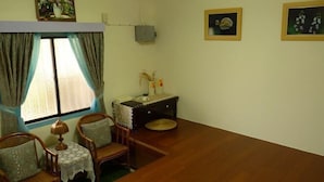 Una habitación con una mesa de comedor de madera, dos sillas de mimbre, una mesita con mantel de encaje, un jarrón decorativo y dos cuadros en la pared.