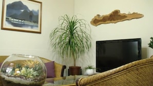 Una sala de estar con un sofá, una mesa de centro de vidrio, una planta en maceta, un acuario, un cuadro enmarcado y un televisor de pantalla plana.