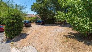 Ein Schotterweg führt zu einem geparkten Auto in einer Wohngegend mit Bäumen und einem Haus im Hintergrund.