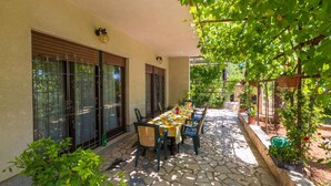 Eine Terrasse im Freien mit einem langen Esstisch, umgeben von Stühlen, und einer Pergola mit Kletterpflanzen.