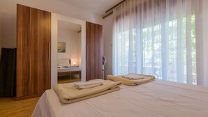Ein Schlafzimmer mit zwei Betten, einem Holzschrank, einem Spiegel und einem Fenster mit Vorhängen.